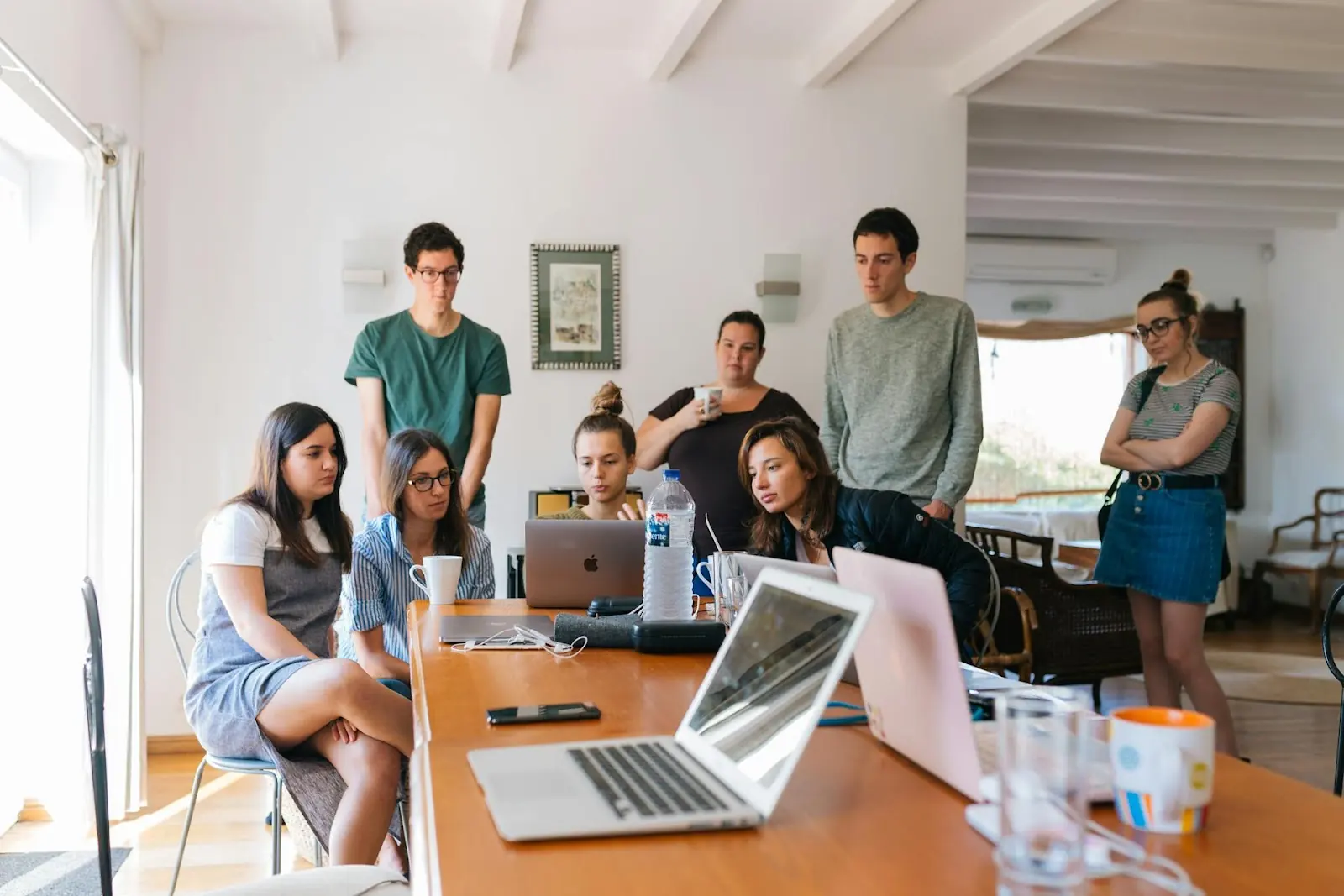 A few people gathered around a table with one person showing the others something on her laptop screen