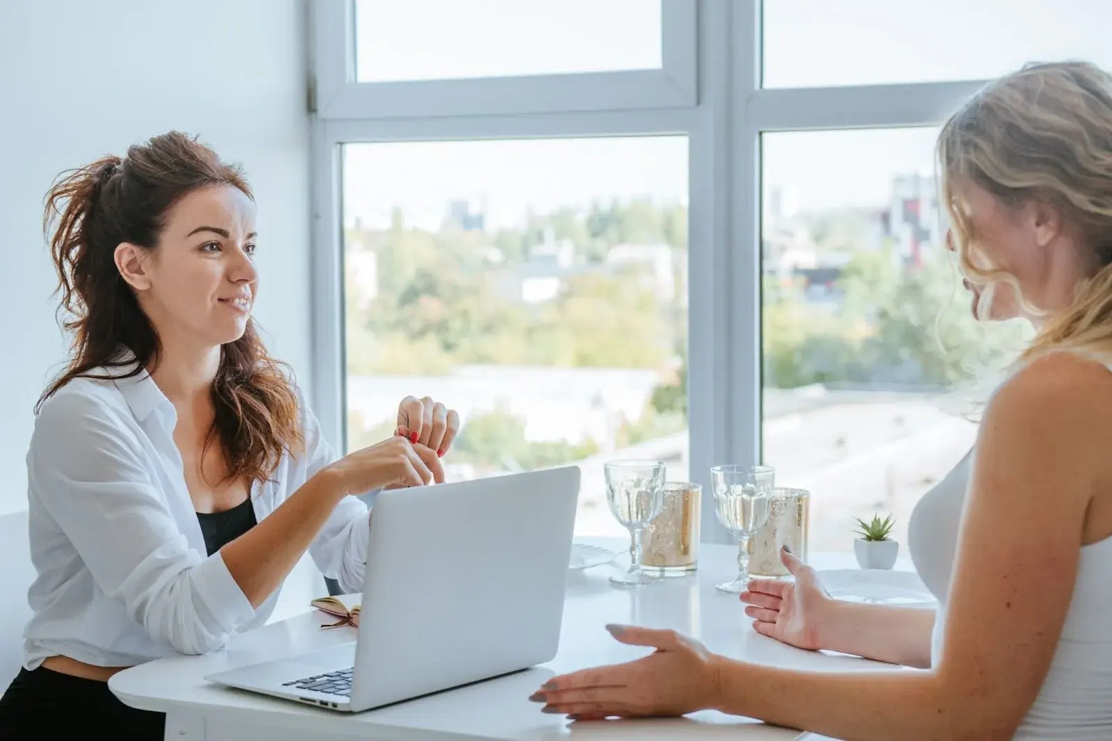 Two women seated across a table with a laptop between them