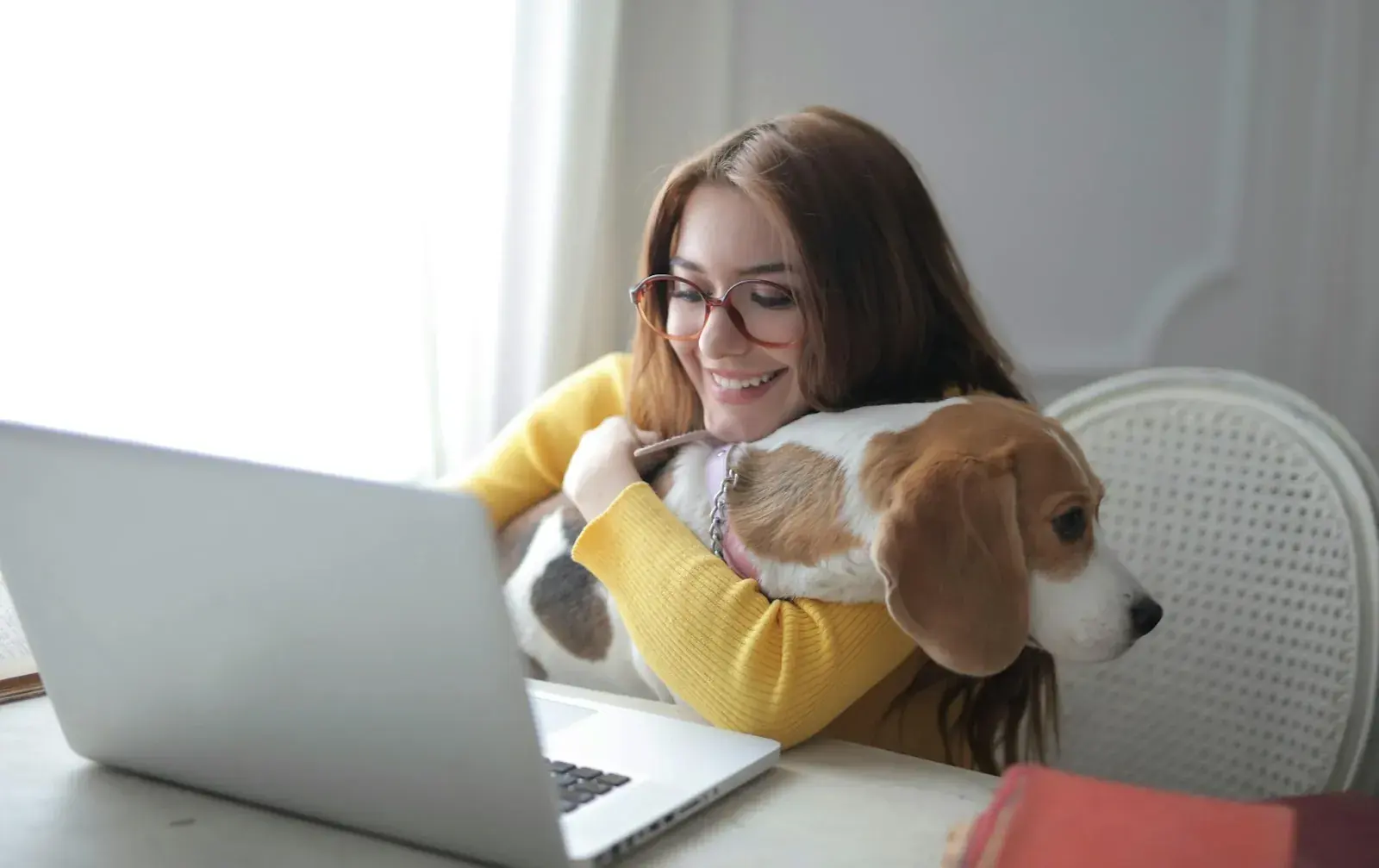 A woman in front of a computer, hugging a dog‍