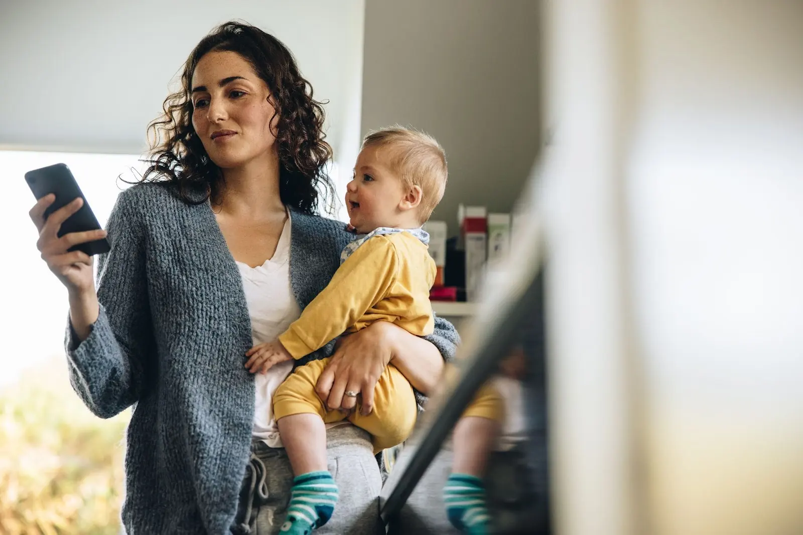 A woman holding a baby in one hand and a phone in the other
